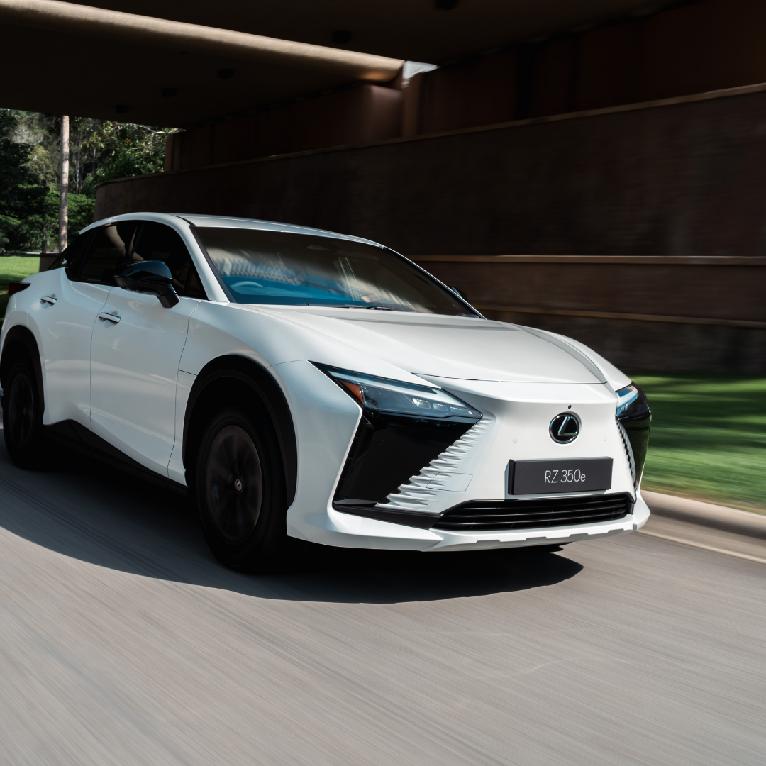 White Lexus RZ 350e driving along a tree-lined road